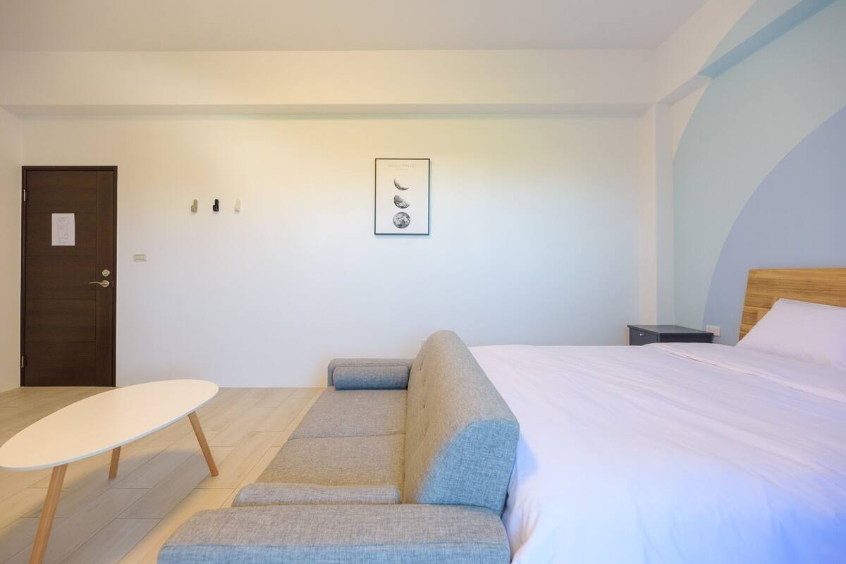 A modern bedroom with a bed, a sofa, a small table, and a nightstand.