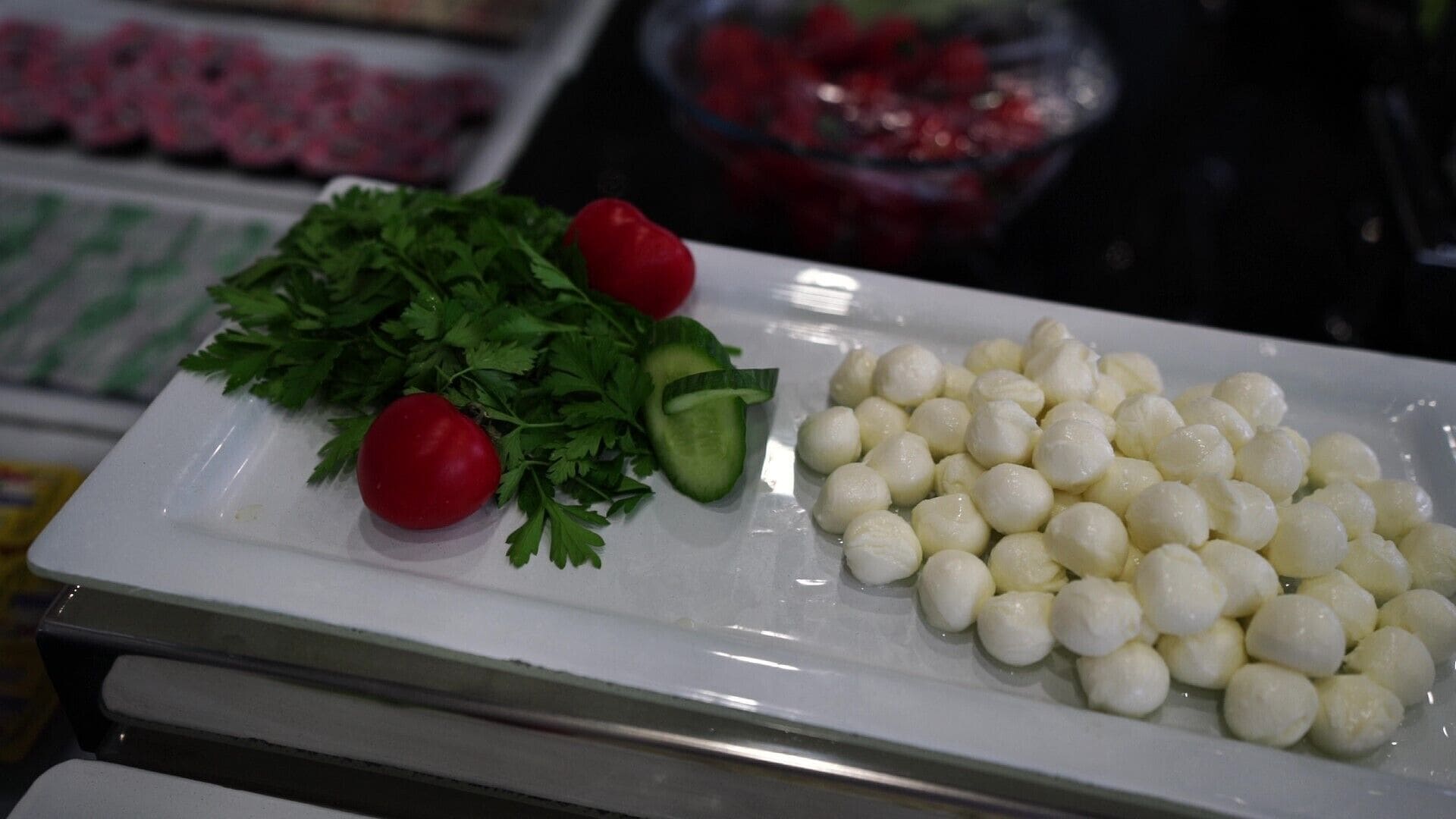 Un plato blanco con perejil, tomate y bolas de mozzarella.