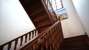 Una scala in legno con corrimano che conduce a un pianerottolo con una finestra e un dipinto di paesaggio.