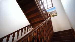 A wooden staircase with a handrail, leading to a landing with a window and a landscape painting. - VE HOTELS KAPADOKYA (Nevsehir)