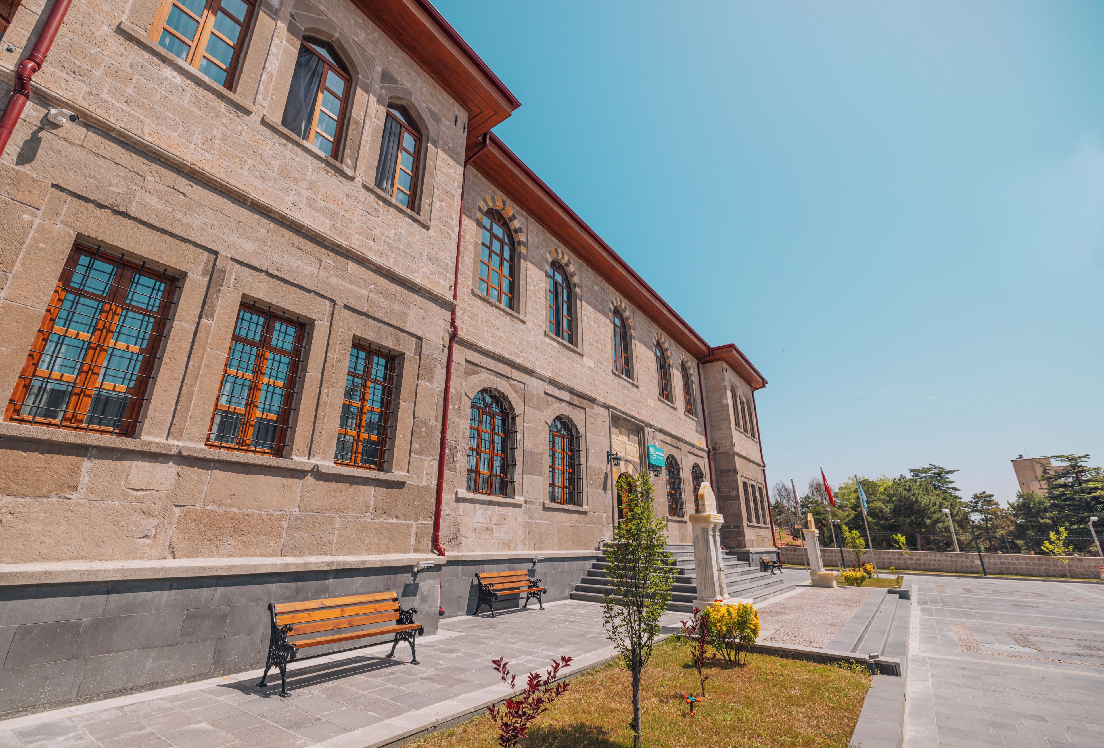 A building with large windows, a stone facade, and a paved area with benches.