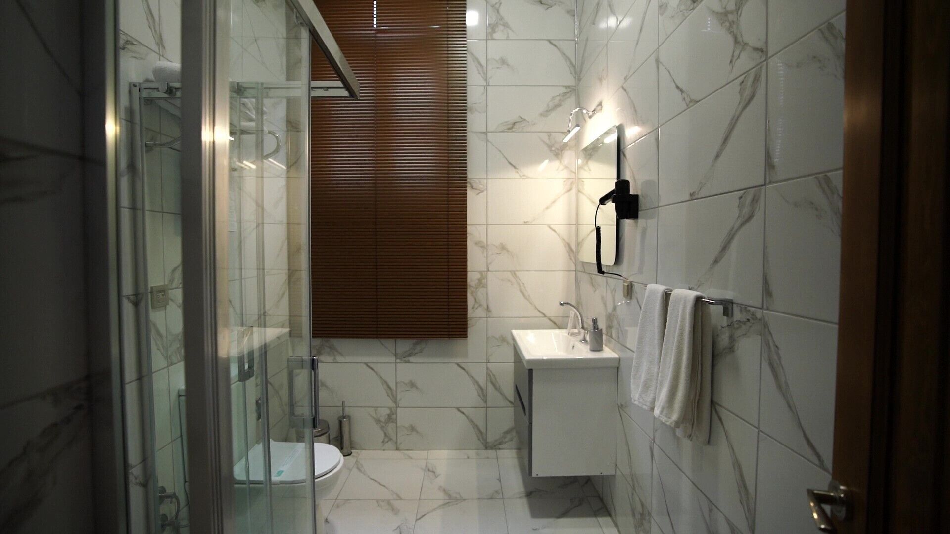 A modern bathroom with a glass-enclosed shower, a toilet, a sink, and a towel rack.