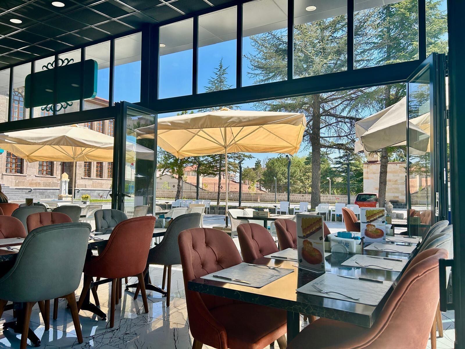 An outdoor dining area with tables and chairs, large umbrellas, and a view of the surrounding buildings and trees.