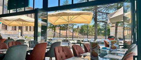 An outdoor dining area with tables and chairs, large umbrellas, and a view of the surrounding buildings and trees.