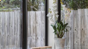 A window with a view of a wooden fence, a potted orchid, and three containers labeled "Sugar," "Tea," and "Coffee." - Nature's Edge Hideaway (Ocean Grove)