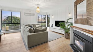 A modern living room with a sofa, fireplace, and large windows. - Nature's Edge Hideaway (Ocean Grove)