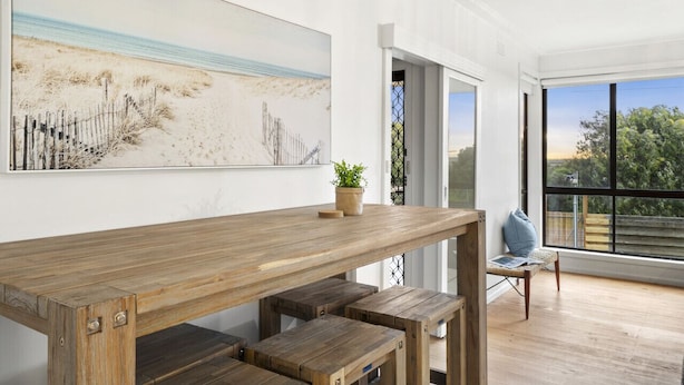 A wooden dining table with benches, a potted plant, and a chair with a cushion. - Nature's Edge Hideaway (Ocean Grove)