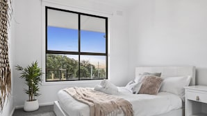 A bedroom with a large window, a bed, a bedside table, and a potted plant. - Nature's Edge Hideaway (Ocean Grove)
