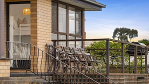 A modern building with a brick facade, large windows, and a balcony with wooden chairs. - Nature's Edge Hideaway (Ocean Grove)