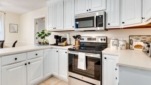 Una cocina moderna con armarios blancos, un microondas de acero inoxidable, un horno y una cafetera.