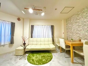 Ein modernes Wohnzimmer mit einer Couch, einem kleinen Tisch, einem grünen Teppich und einem Essbereich.