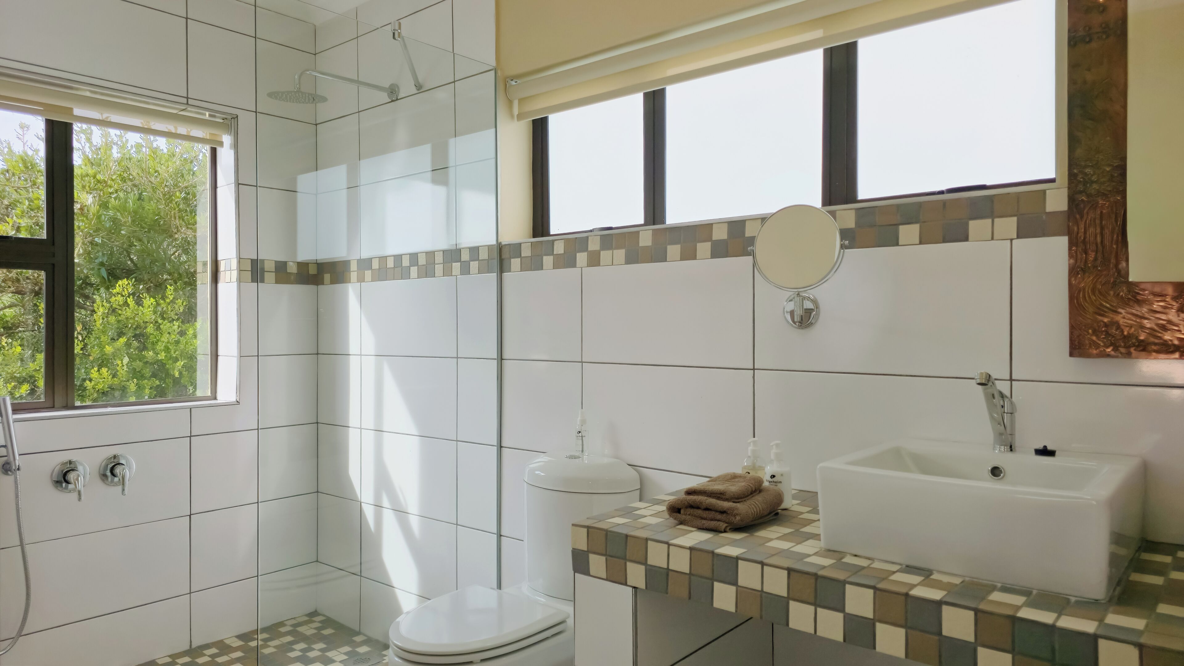 Un baño con ducha, inodoro, lavamanos y ventana con vistas al verdor.