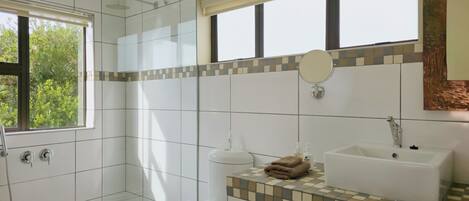 Un baño con ducha, inodoro, lavamanos y ventana con vistas al verdor.