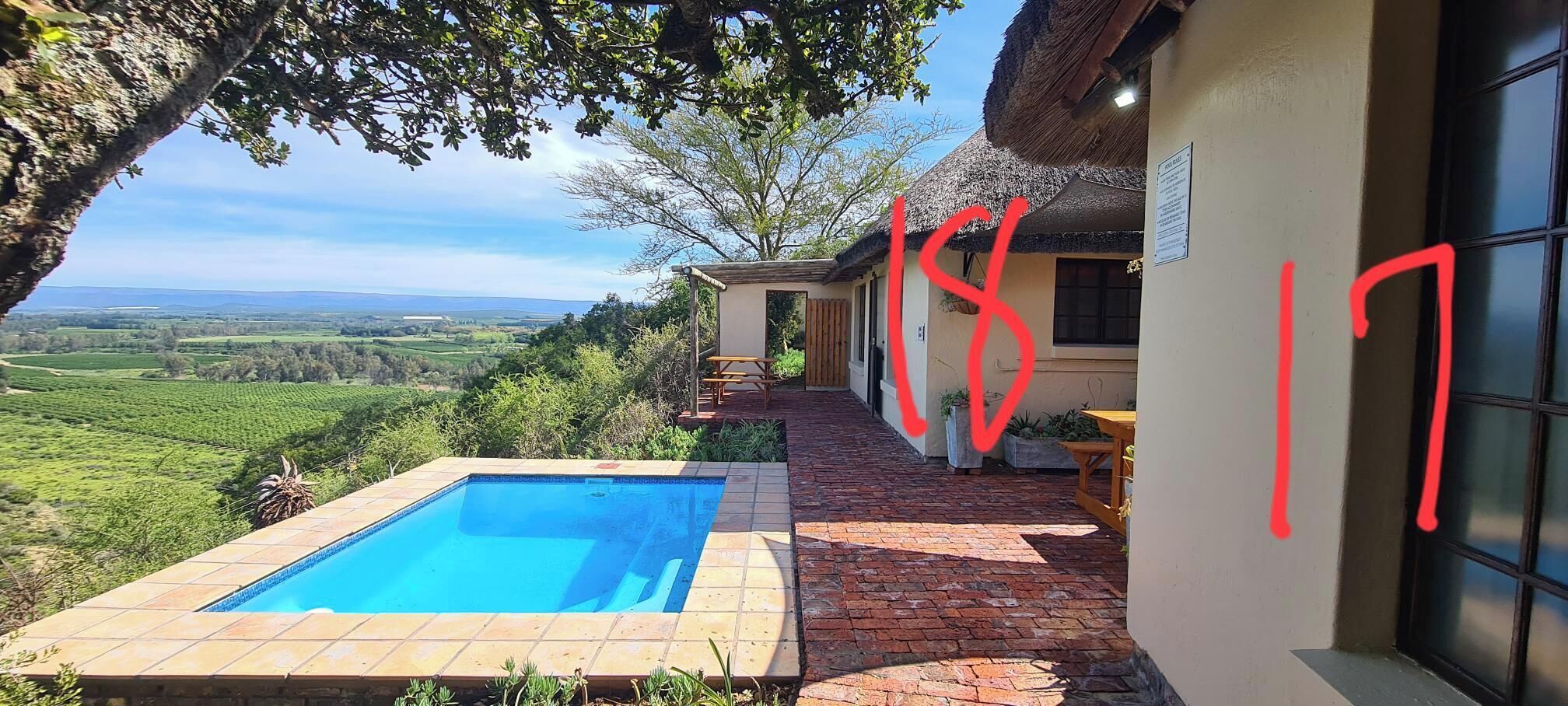 A pool area with a view of the countryside, a patio with a table and chairs, and a building with a thatched roof.