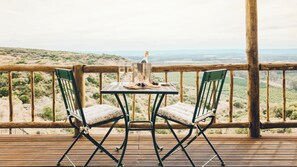 Une terrasse en bois avec deux chaises vertes et une table, une bouteille de champagne et un seau portant l’inscription « SOURCÉ DE PARIS ».