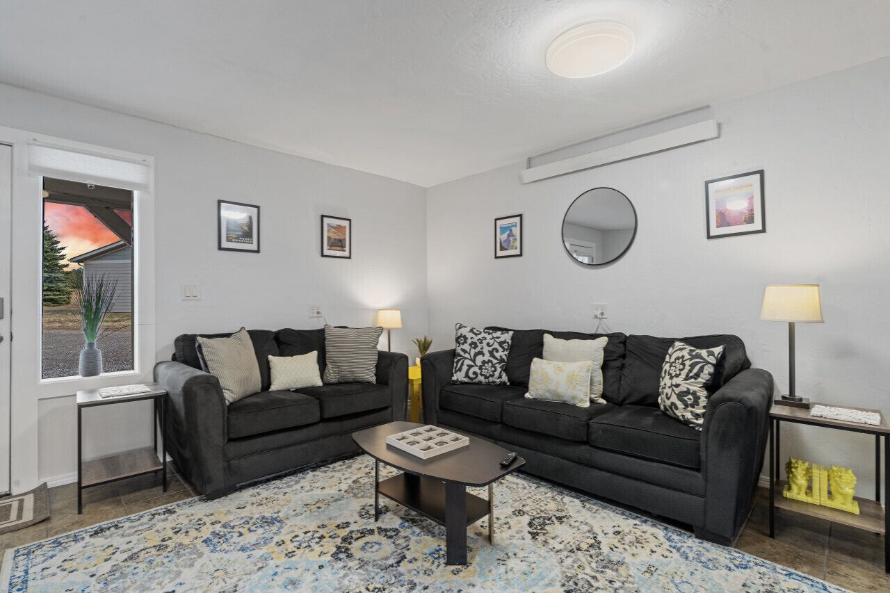 A living room with two black sofas, a coffee table, a rug, and framed pictures on the walls.
