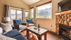 A cozy living room with a fireplace, large windows with mountain views, and comfortable seating. - "Rundle Vista" at Canmore Crossing (Canmore)