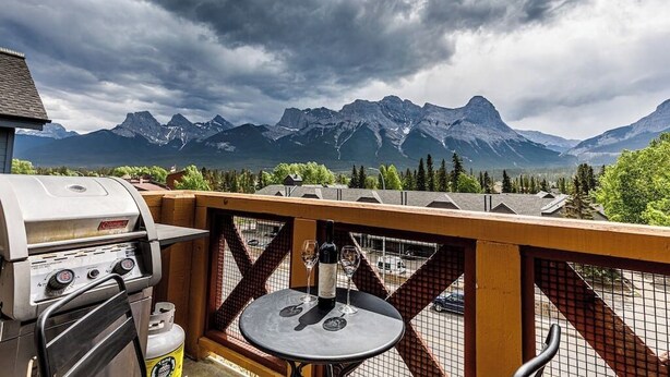 A balcony with a grill and a table with wine glasses, overlooking a mountainous landscape. - "Rundle Vista" at Canmore Crossing (Canmore)