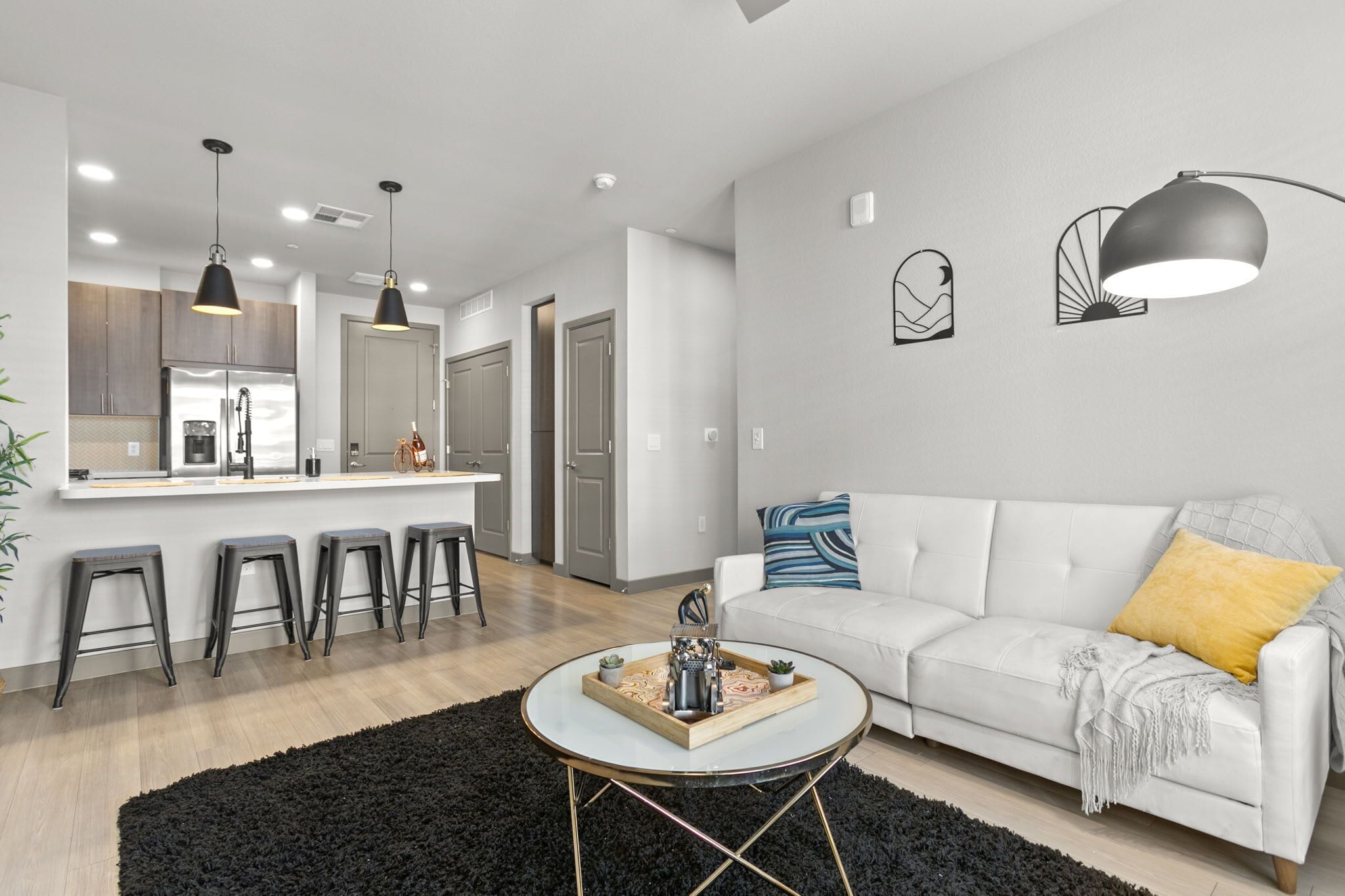 A modern living room with a white sofa, black and yellow cushions, a round coffee table, and a black rug.