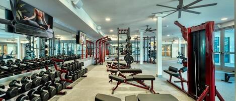 Un gimnasio con filas de mancuernas, bancos y máquinas de pesas.