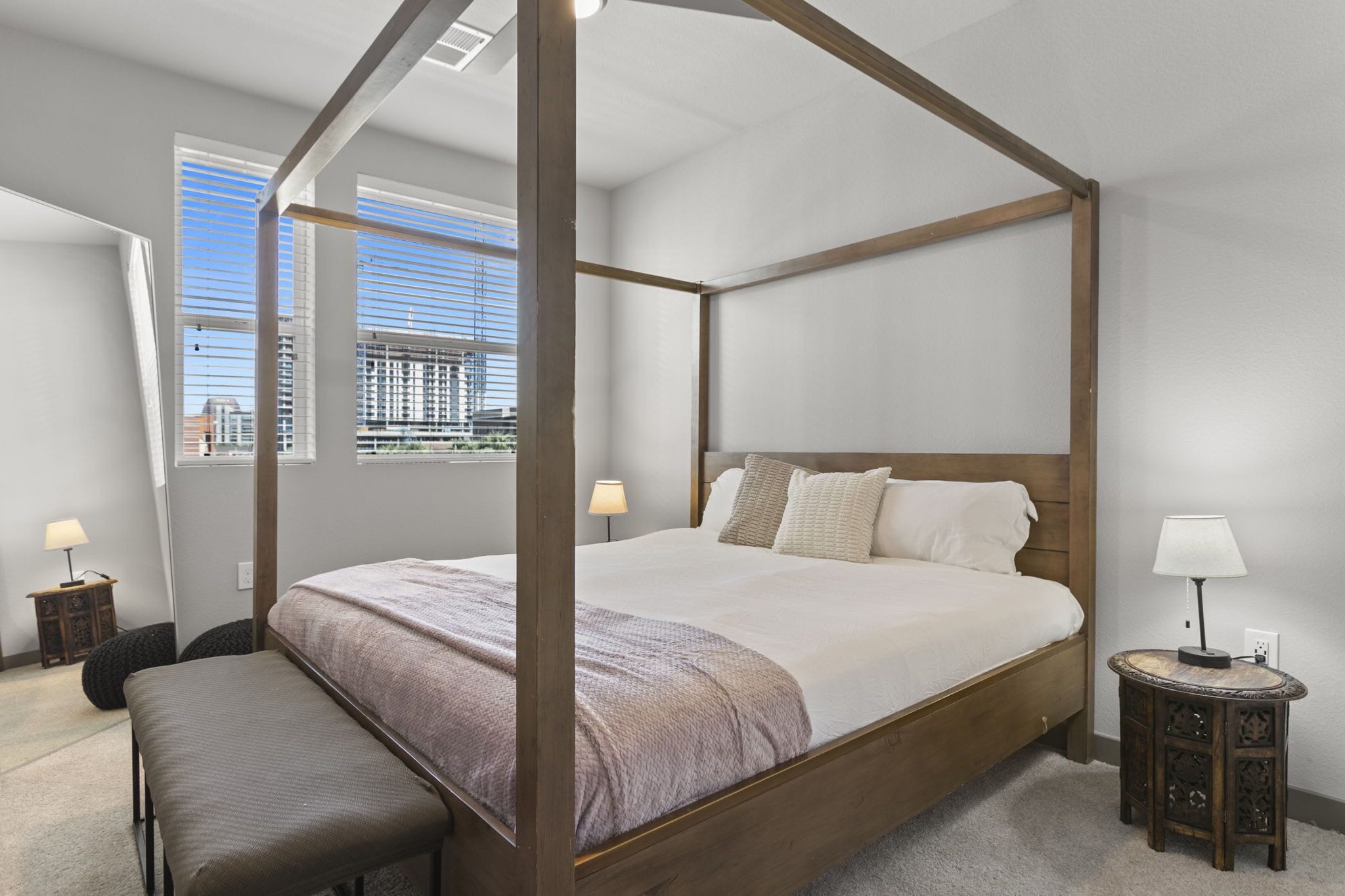 A four-poster bed with a city view, a small bedside table, and a bench.