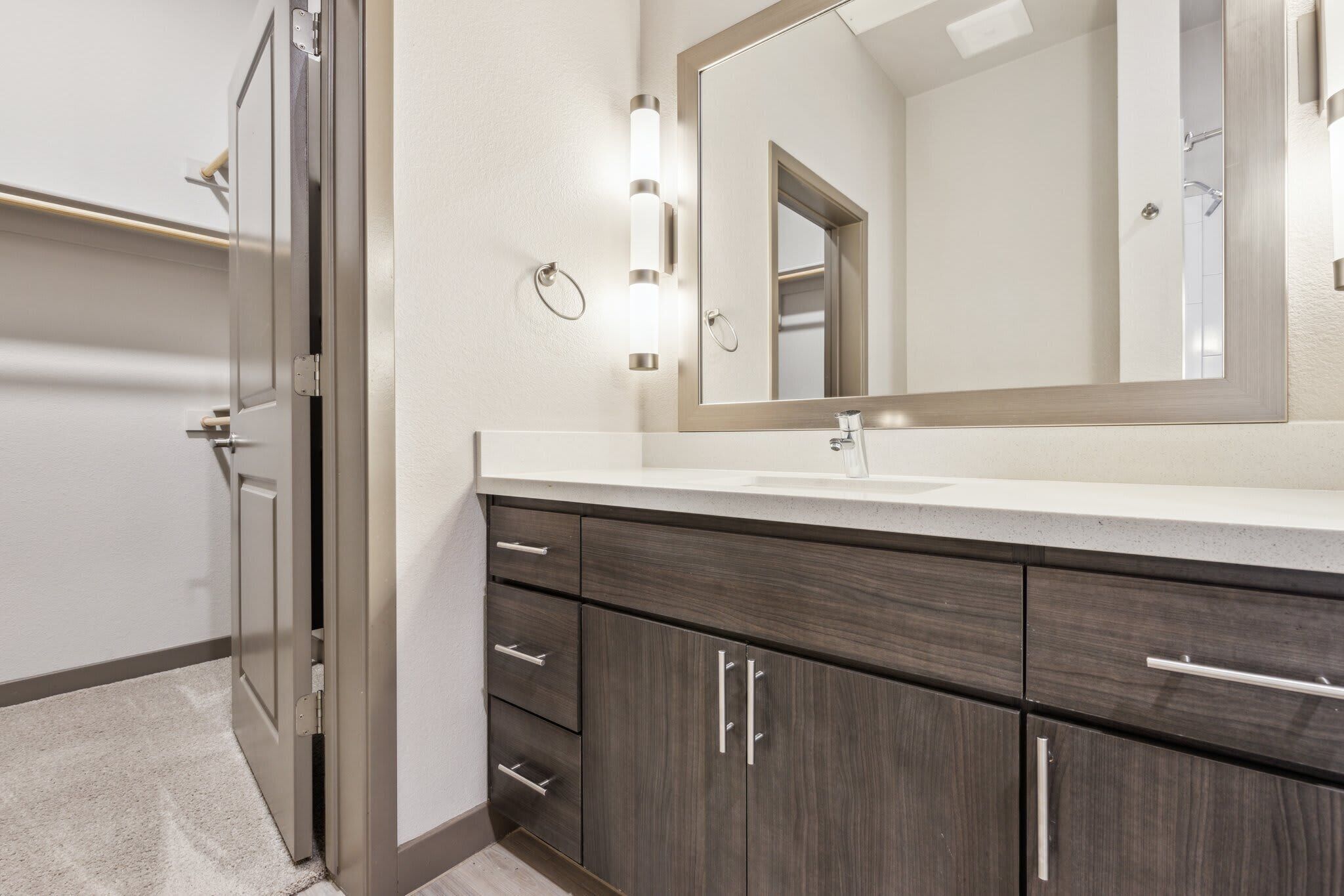 A bathroom with a double vanity, a large mirror, and a light fixture above the mirror.