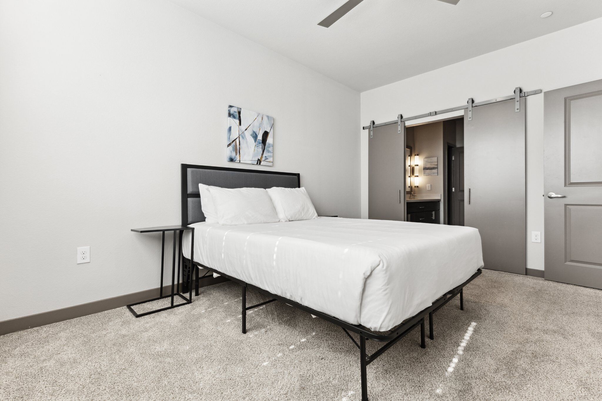 Een moderne slaapkamer met een bed, een nachtkastje, een wanddecoratie in abstractie en een schuifdeurkast.