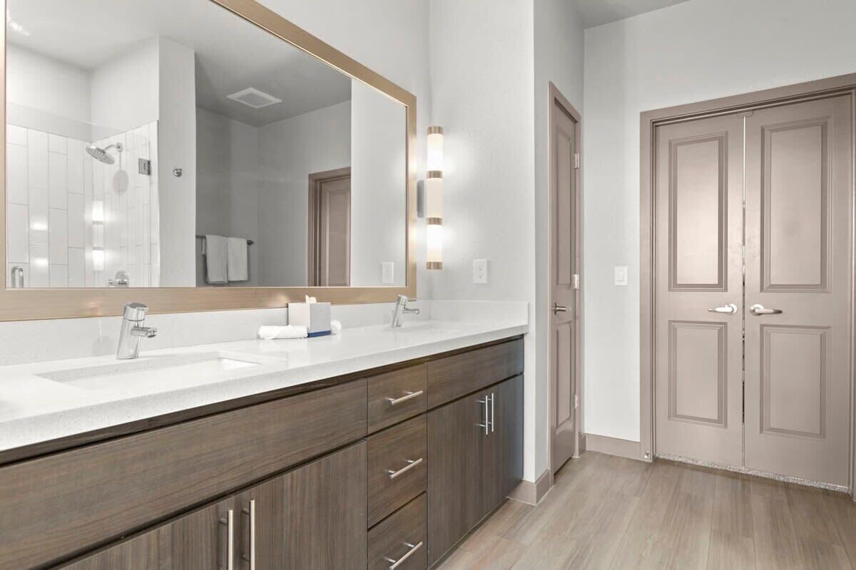 A modern bathroom with a large mirror, a sink, and a shower.