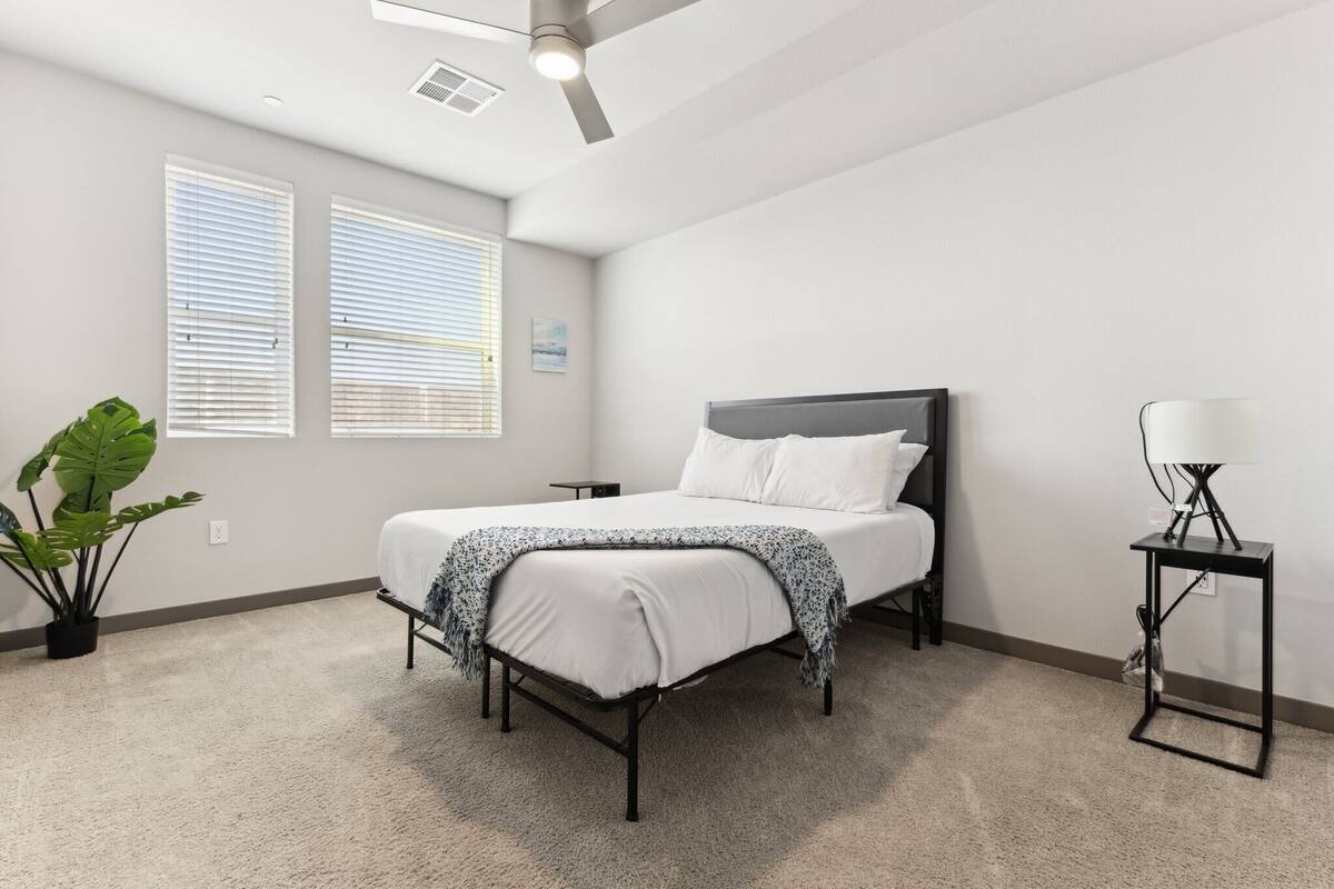 A bedroom with a bed, a ceiling fan, a nightstand, a lamp, and a potted plant.