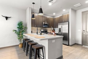 A modern kitchen with a central island, bar stools, a microwave, a refrigerator, and a potted plant. - CozySuites at Downtown Phoenix (Phoenix)