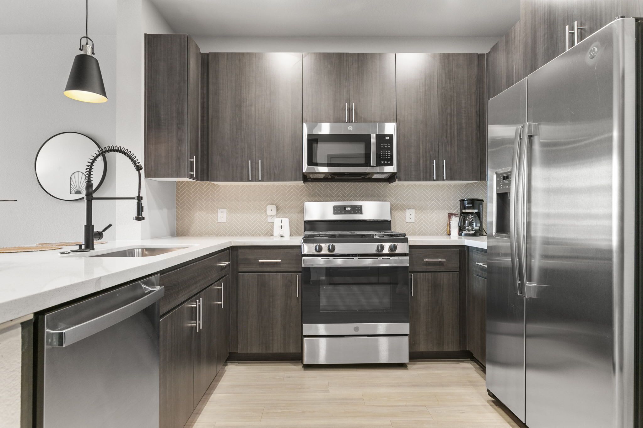 A modern kitchen with dark wood cabinets, stainless steel appliances, and a herringbone-patterned backsplash.