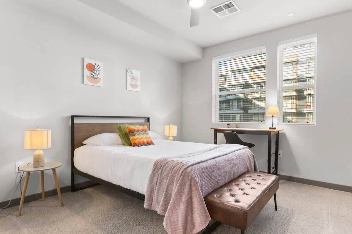 A modern bedroom with a bed, bedside tables, a desk, and a window with blinds.