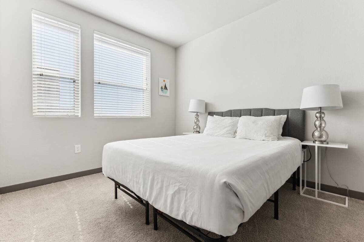 A bedroom with a bed, two bedside lamps, a nightstand, and a window with blinds.