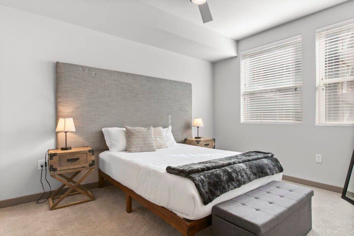 A bedroom with a large bed, bedside lamps, a wooden nightstand, a bench, and a ceiling fan.