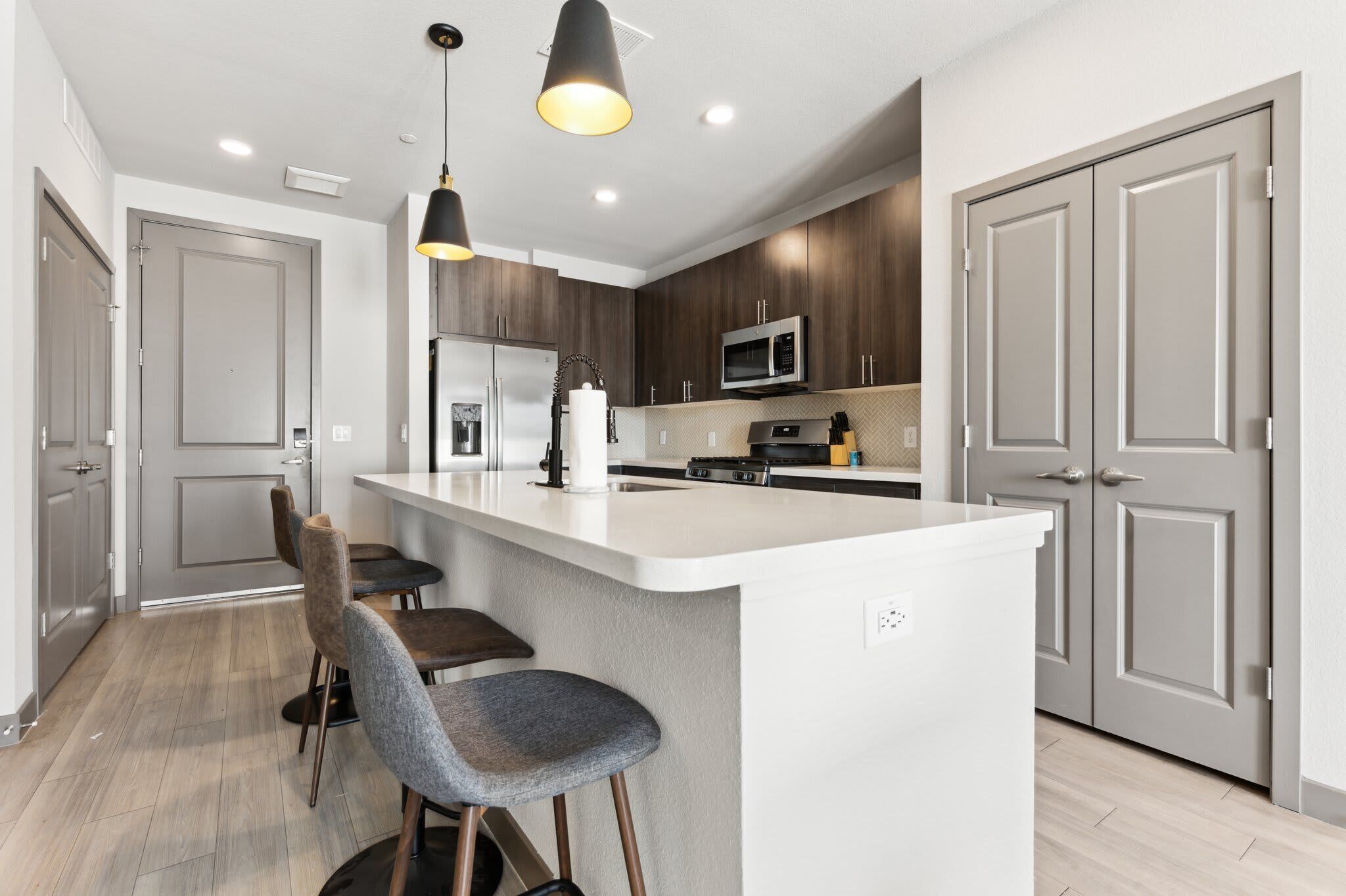 A modern kitchen with a central island, bar stools, a microwave, and a refrigerator.