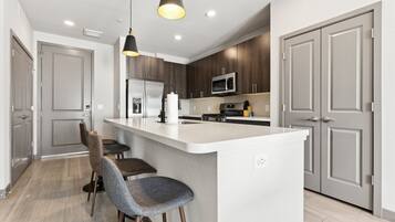 A modern kitchen with a central island, bar stools, a microwave, and a refrigerator.