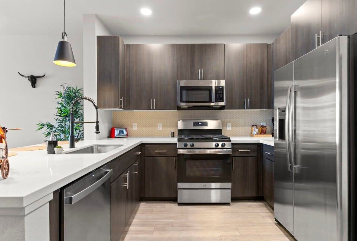 Una cocina moderna con electrodomésticos de acero inoxidable, armarios de madera oscura y encimera blanca.