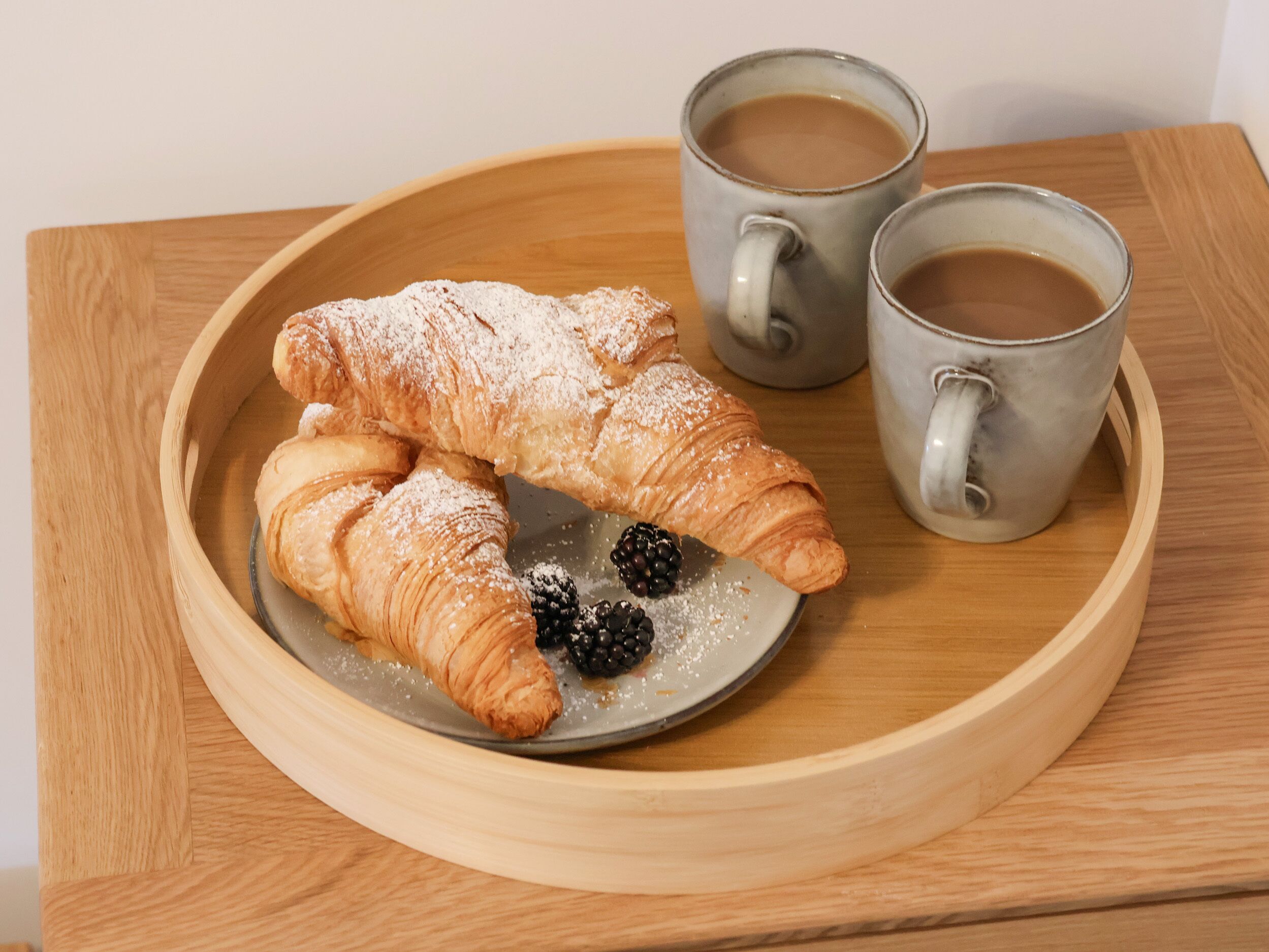 A wooden tray with two pastries and two mugs on a table.