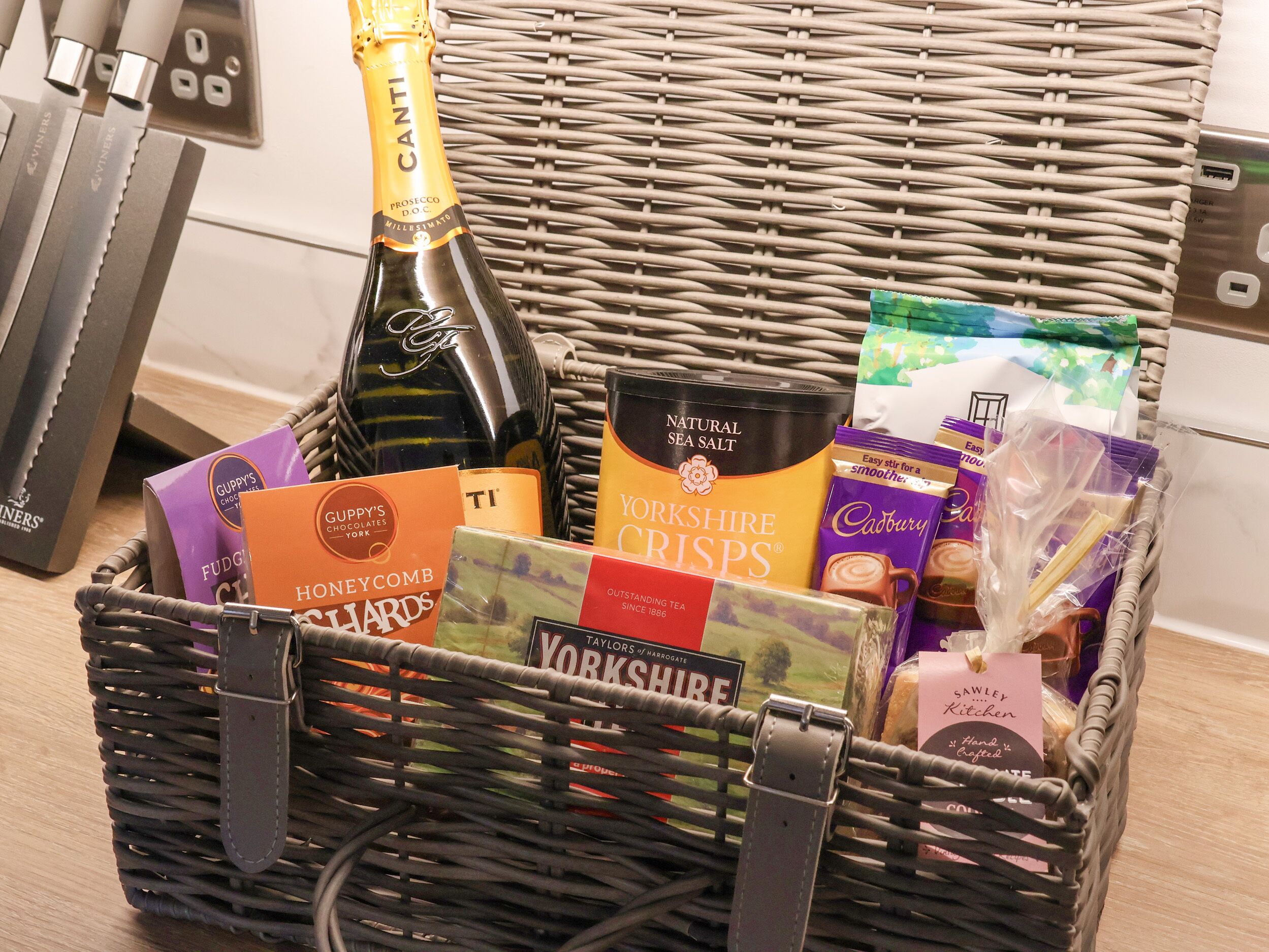 A wicker basket filled with various food items including a bottle of champagne, chocolate bars, and tea.