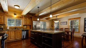 A spacious kitchen with wooden cabinets, a stainless steel refrigerator, and a large island with a sink. - Browning Lodge Retreat! (Duck Creek Village)