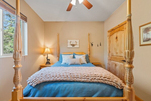 A four-poster bed with a blue blanket, a bedside lamp with a deer figurine, and a wooden wardrobe. - PET-FRIENDLY FOREST RETREAT CABIN | HOT TUB, FIRE-PIT, & A/C (Duck Creek Village)