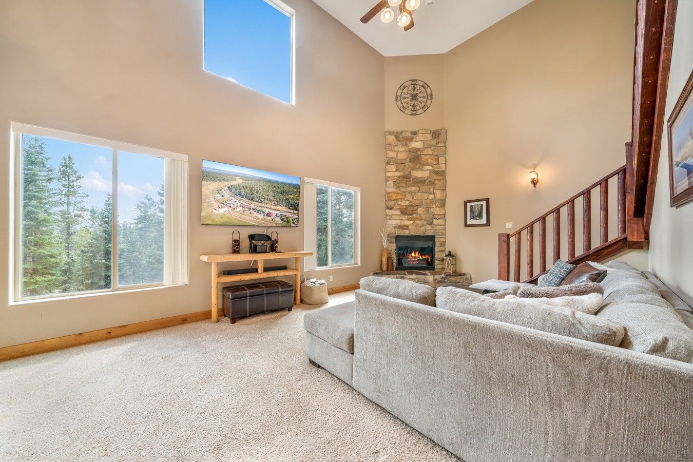 A spacious living room with a stone fireplace, large windows, a high ceiling, and a cozy seating area.