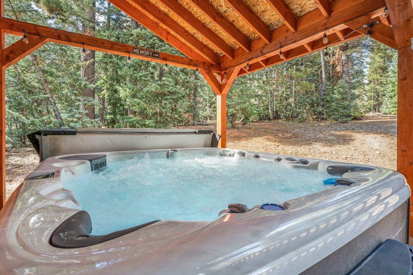 Ein Whirlpool unter einer hölzernen Pergola in bewaldeter Landschaft.