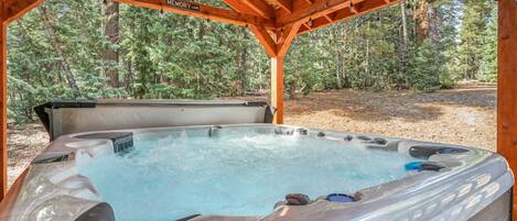 Ein Whirlpool unter einer hölzernen Pergola in bewaldeter Landschaft.