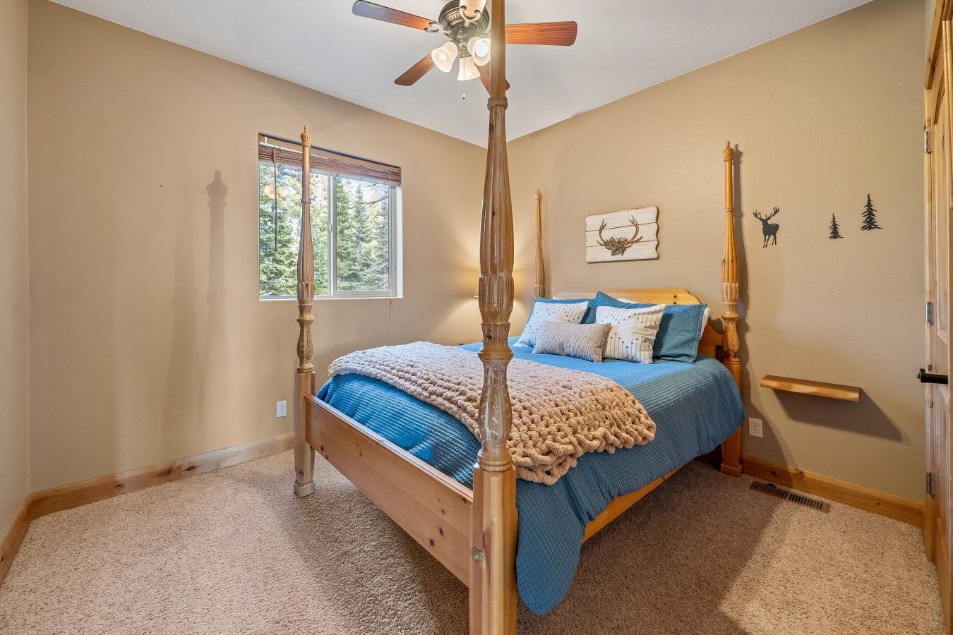 A bedroom with a four-poster bed, a ceiling fan, a window with blinds, and wall decorations including antlers and a deer silhouette.