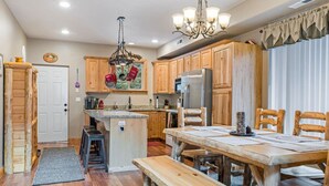 A rustic kitchen with wooden cabinets, a central island, and a dining area with a bench. - PET-FRIENDLY FOREST RETREAT CABIN | HOT TUB, FIRE-PIT, & A/C (Duck Creek Village)