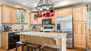 A modern kitchen with wooden cabinets, granite countertops, stainless steel appliances, and a hanging pot rack. - PET-FRIENDLY FOREST RETREAT CABIN | HOT TUB, FIRE-PIT, & A/C (Duck Creek Village)