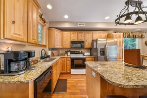 A kitchen with wooden cabinets, granite countertops, a coffee maker, a refrigerator, and a microwave. - PET-FRIENDLY FOREST RETREAT CABIN | HOT TUB, FIRE-PIT, & A/C (Duck Creek Village)