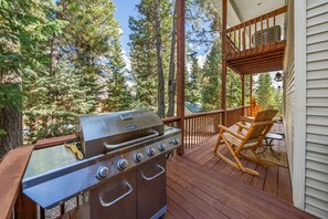 A wooden deck with a grill and a rocking chair. - PET-FRIENDLY FOREST RETREAT CABIN | HOT TUB, FIRE-PIT, & A/C (Duck Creek Village)