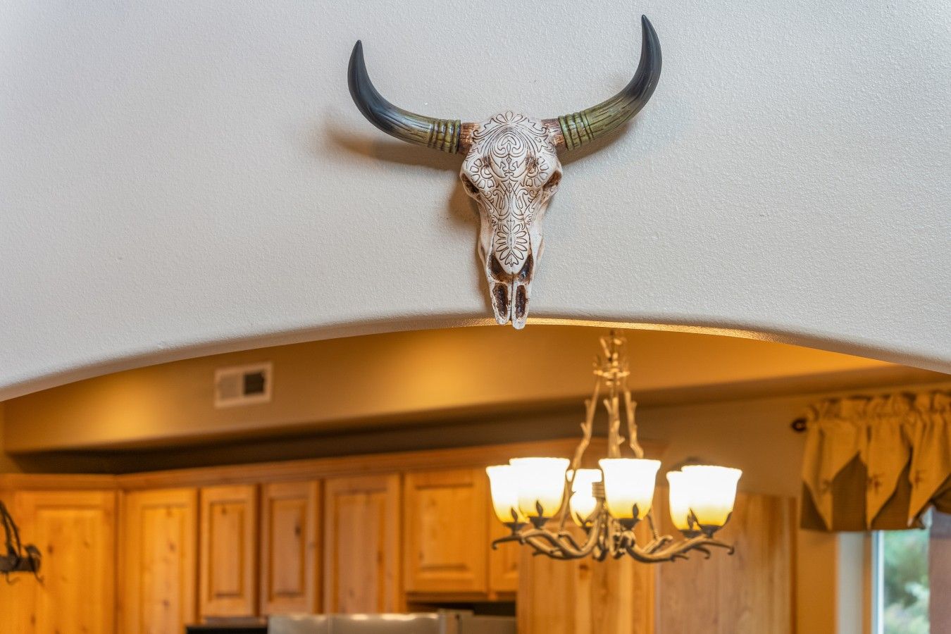 A kitchen with wooden cabinets, a chandelier, and a bull skull mounted on the wall.